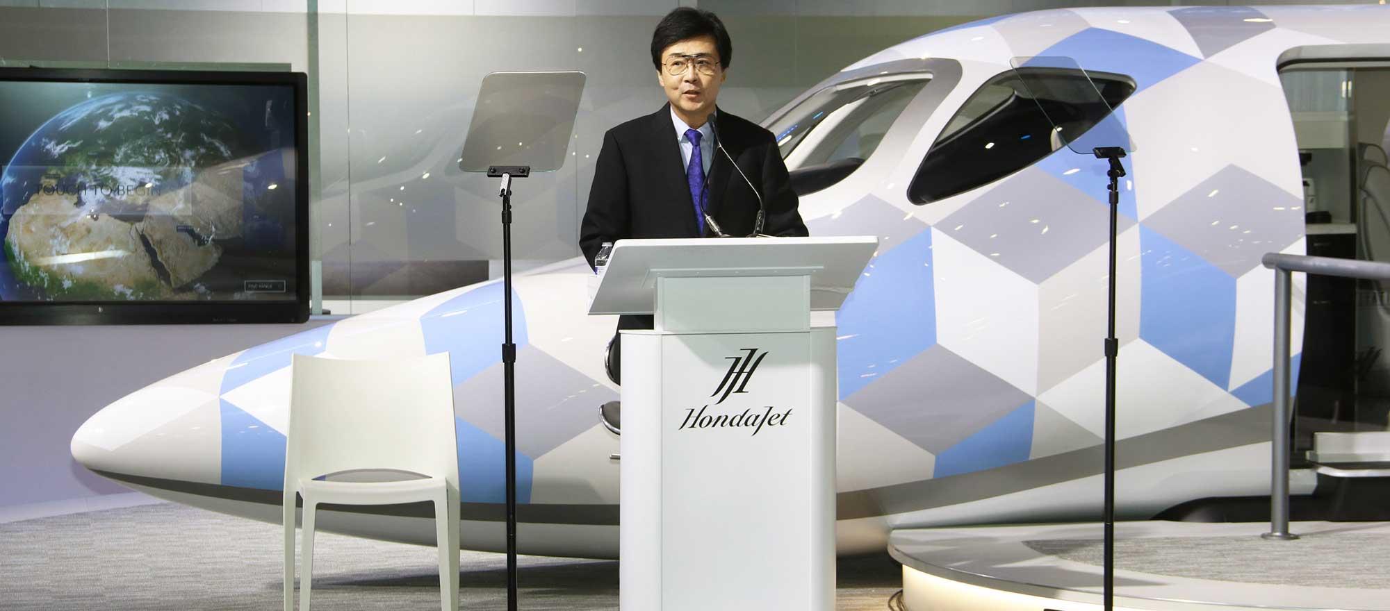 Honda Aircraft CEO, Michimasa Fujino standing at a podium in front of HondaJet 2600 mockup